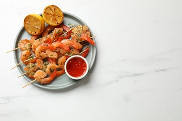 Delicious grilled shrimp skewers served with sauce and lemon on white marble table, top view. Space for text