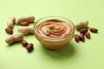 Tasty peanut butter in bowl and groundnuts on green table