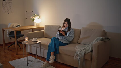 Businesswoman reading tablet evening at room. Serious woman working sitting sofa