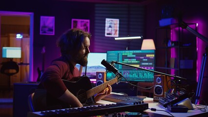 Artist with condenser microphone composing a song on guitar, working on mixing and mastering music. Producer recording tunes and adding sound effects in post production. Camera B.