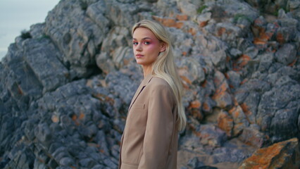 Fashionable blonde looking camera at ocean cliff. Closeup attractive woman model