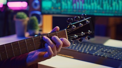 Professional songwriter playing guitar and using soundboard for mixing and mastering tracks. Producer composing a song with audio equipment at home recording studio, equalization tools. Camera A.