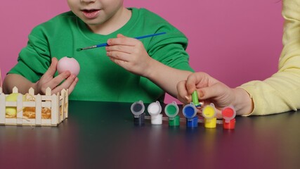 Fototapeta premium Young adorable kids coloring easter eggs with watercolor paint, creating lovely designs to celebrate spring holiday. Cheerful brother and sister painting festive decorations in studio. Camera A.