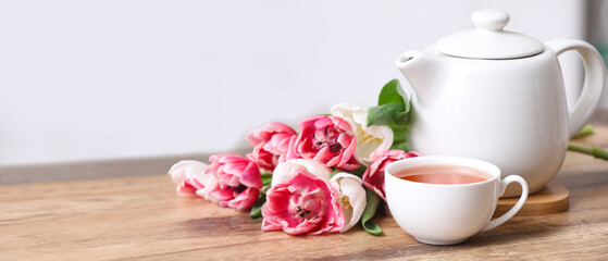 Cup of hot brewed tea, pot and flowers on table against blurred background