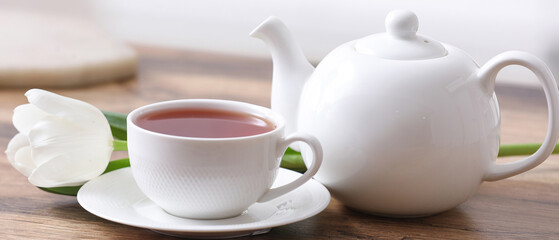 Hot cup of tea, pot and tulip on table against blurred background