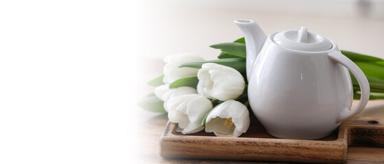 Hot brewed pot of tea and tulips on table against blurred background