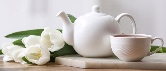 Tea pot and cup near tulips on table against blurred background