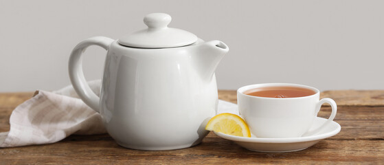 Cup of hot tea, teapot and fabric napkin on wooden table near beige wall