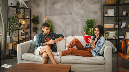 Obraz premium relaxed couple girlfriend read a book and boyfriend use mobile phone