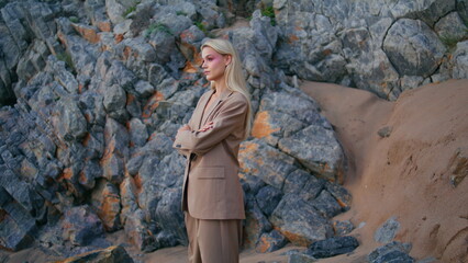 Beach girl modeling rocks at sandy shore. Attractive blonde in fashionable suit