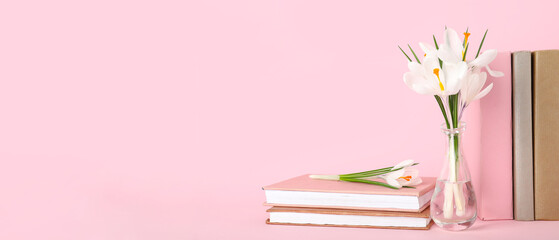 Glass vase with beautiful white crocus flowers and books on pink background
