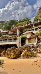 Fototapeta premium Charming houses on a rocky cliffside with thatched roofs, vibrant flowers, and lush greenery. Idyllic tropical setting with a sandy beach, perfect for serene coastal living and nature stock photos