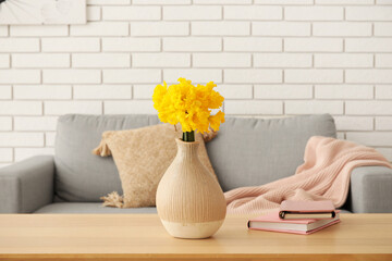 Vase with narcissus flowers and books on table in living room