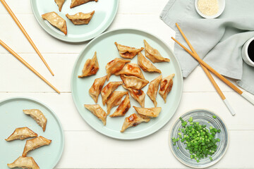 Plates with tasty Chinese jiaozi, onion and sauce on white wooden background