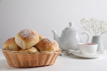 Delicious dough balls with powdered sugar in basket, tea, teapot and gypsophila flowers on white wooden table