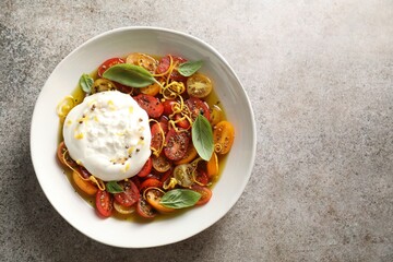 Delicious fresh burrata salad in bowl on gray textured table, top view. Space for text