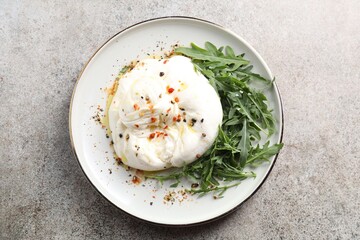 Delicious burrata cheese, arugula and spices on grey table, top view