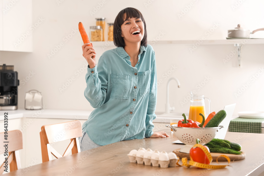 Poster Young woman with carrot in kitchen. Diet concept