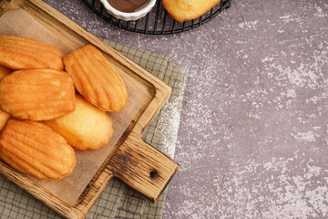 Wooden board with delicious madeleines on grey background
