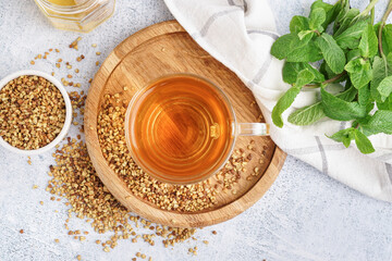Glass cup of tasty buckwheat tea and mint on light background