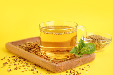 Glass cup of tasty buckwheat tea and mint on yellow background, closeup