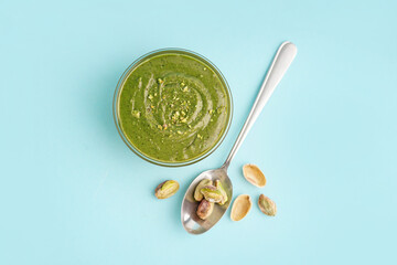 Tasty pistachio paste in bowl and spoon on blue background