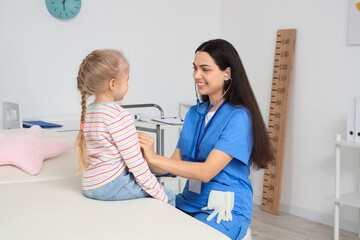 Female pediatrician with stethoscope listening to little girl in clinic