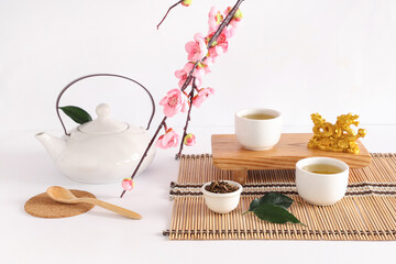 Wooden stand with teapot, cups, dry tea and sakura branch on white background