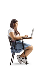 Female teenager sitting in a school chair and using a laptop computer