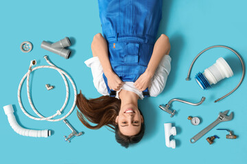 Happy young female plumber with different plumbing items lying on blue background