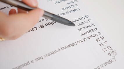 Obraz premium Female circles correct answers in standard exam test paper with black pen. Student filling up the answer sheet, choosing right answer, macro shot.
