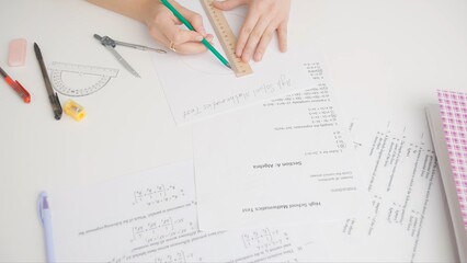 Female draws correct answer in geometry exam test paper with pencil and ruler. Student filling up the answer sheet, writing right answer, top view shot.