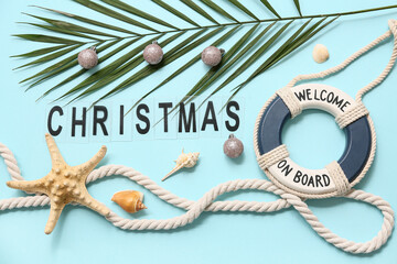 Fototapeta premium Palm branch with Christmas balls, decor lifebuoy, starfish, rope and word CHRISTMAS on blue background. Top view