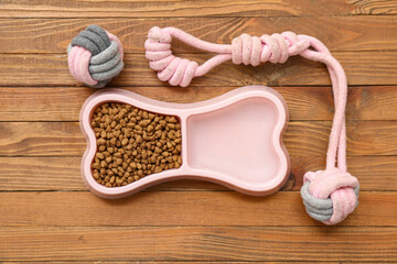 Bowl with dry food near chew toy on brown wooden background
