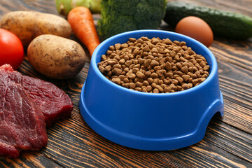 Bowl with healthy dry pet food and vegetables on brown wooden background