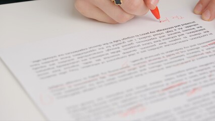 Obraz premium Professional school or college teacher grades a homework exam papers of students. Woman checks essay, crosses wrong words, corrects it with red pen.