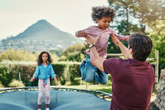 Happy kids, trampoline and jump in outdoor, playing and father helping in backyard of home. Children, daddy and energy for fun activity in childhood, garden and bounce movement for bonding together