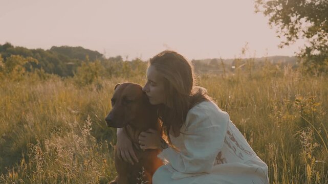 young cheerful woman playing with her dog outdoors in beautiful countryside field. Female and ridgeback dog walking and having fun