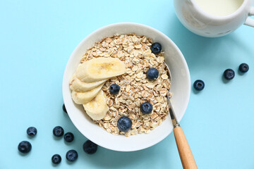 Bowl with raw oatmeal, banana and berries on blue background, closeup