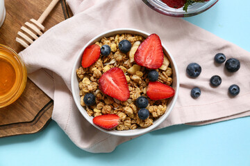 Napkin, bowl with tasty granola and berries on blue background, closeup