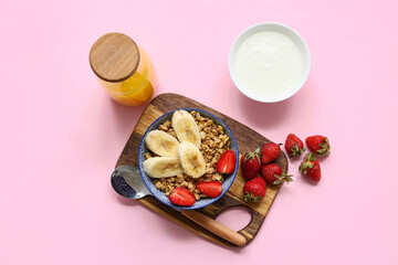 Wooden cutting board, bowl with tasty granola, banana and strawberries on pink background
