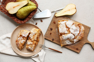 Wooden board and plate with pieces of tasty pear strudel on grey background
