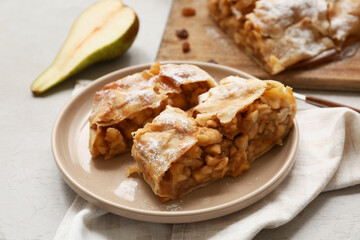 Plate with pieces of tasty pear strudel and napkin on grey background