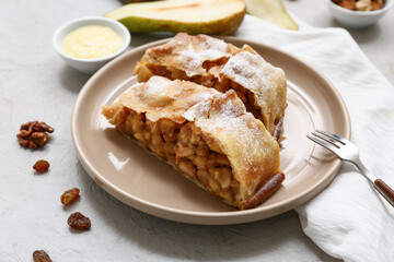 Plate with pieces of tasty pear strudel, nuts and fork on grey background