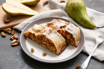 Plate with pieces of tasty pear strudel and fork on grey grunge background