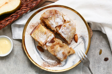 Plate with pieces of tasty pear strudel on grunge grey background