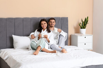 Happy young couple with cups of coffee sitting in bedroom