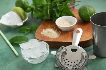 Wooden cutting board, strainer and ingredients for mojito on green background, closeup