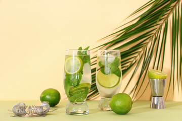 Glasses of fresh mojito with tropical leaves and cocktail strainer on green table against beige background