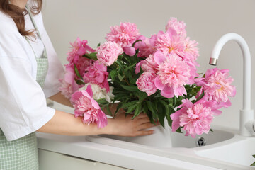Young woman and vase with peony flowers in sink at home